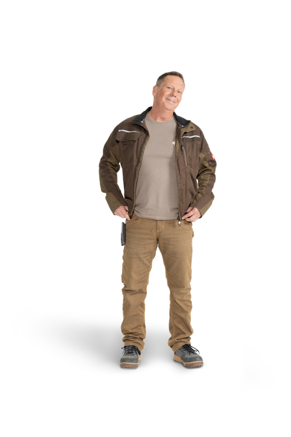 Ein Mann mit olivfarbener Arbeitsjacke, Cargo-Hose und grauem T-Shirt.