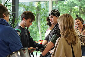 Man siehr eine Gruppe junger Menschen, ein Junge misst einem anderen den Blutdruck.