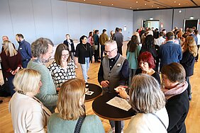 In einem großen Saal sitzen 350 Teilnehmende auf Stühlen, auf der Bühne stehen zwei Personen, die etwas erklären. 