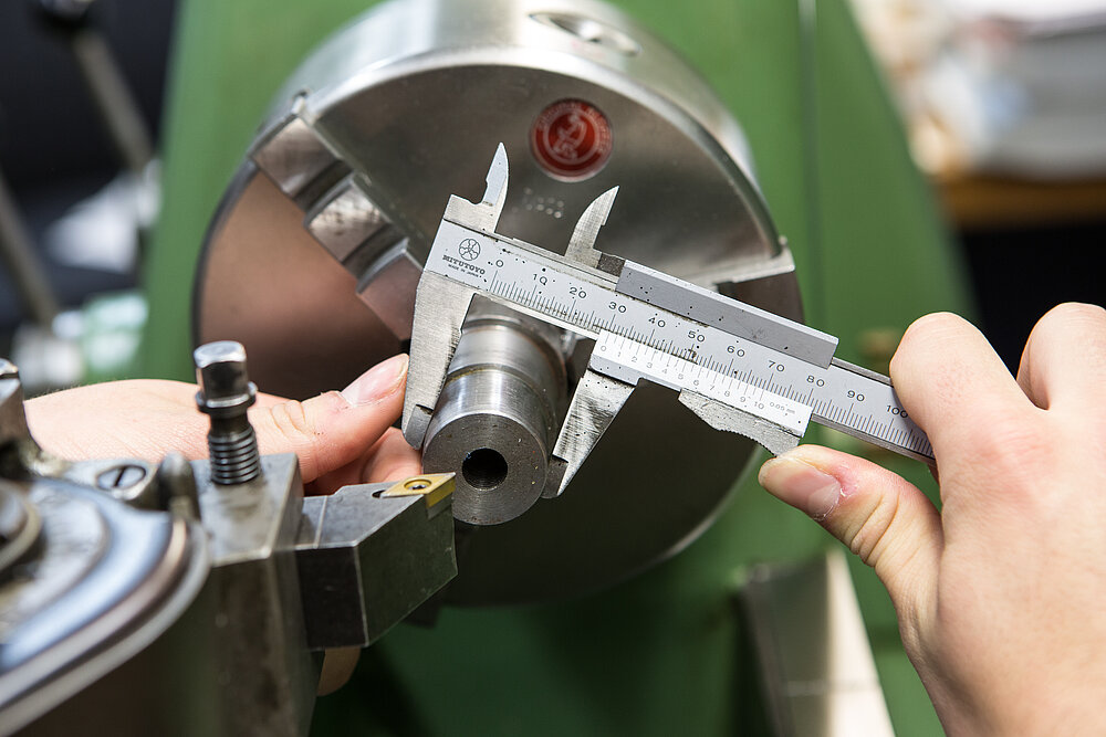 Zwei Hände hantieren an einer Anlagemaschine mit Werkzeug. 