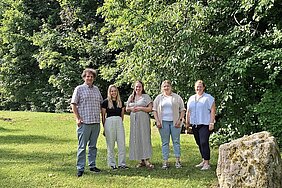 Ein großer Mann und vier Frauen stehen nebeneinander auf einer grünen Wiese.