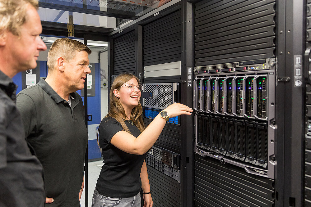 Eine junge Frau und zwei Männer stehen in einem Serverraum.