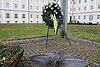 Am Mahnmal Offenes Haus ist ein geschmückter Kranz aufgestellt. Im Hintergrund ist das Kloster Bad Schussenried zu sehen.