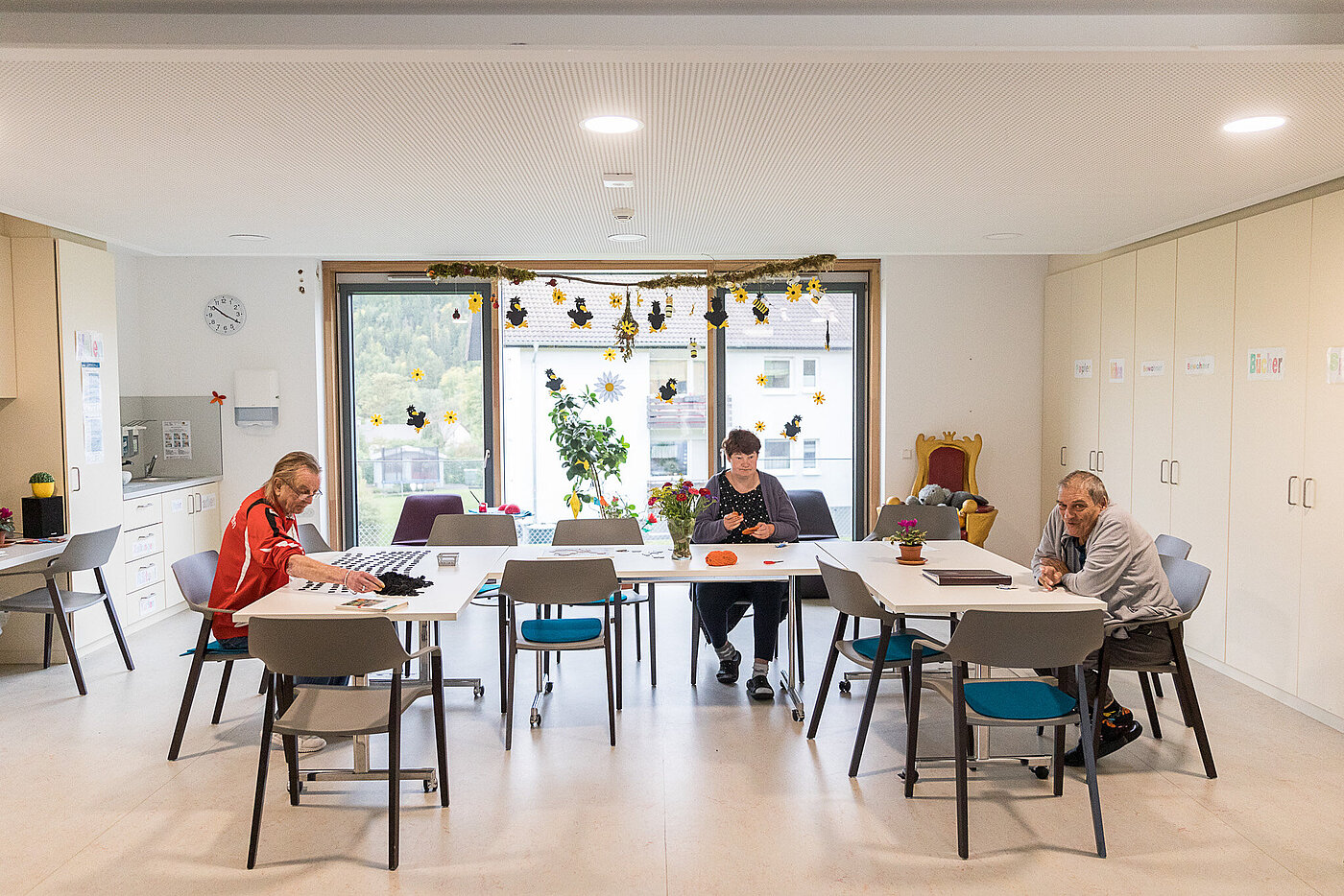 In einem hellen Raum stehen Tische in U-Form. An den Tischen sitzen mehrere Bewohner beim Essen. 