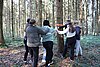 Eine Gruppe junger Menschen stehen im Wald um den Stamm einer großen Tanne, sie haben die Augen verbunden. 
