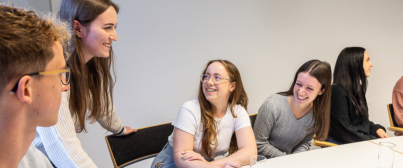 Eine Gruppe junger kaufmännischer Azubis sitzt an einem Tisch und unterhält sich.