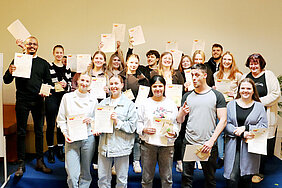 Eine Gruppe junger Menschen blickt lächelnd in die Kamera. Stolz halten sie ihre erhaltenen Zertifikate hoch.