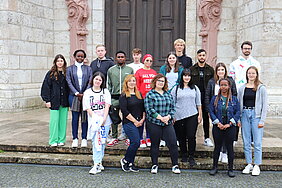 Eine Gruppe junger Menschen steht auf den Stufen des Münsters und schaut freundlich in die Kamera. 